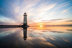 Lighthouse standing in pool of water stunning sunset sunrise reflection reflected in water and sea steps up to building north Wales seashore sand beach still water orange glow golden hour blue hour