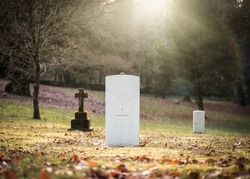Military white British World War One grave with no inscription unknown soldier alone with sun rays shining peaceful and tranquil down through trees from 1914 to 1918 in cemetery church graveyard ww1