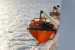 Orange lifeboat on side of north sea ferry boat crossing channel to France or Holland for passengers to escape sinking ship. Emergency life preserve with number 12 on the side in black font.