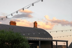 Beautiful sunset over old cow shed barn roof in countryside with chimneys and clouds in view.