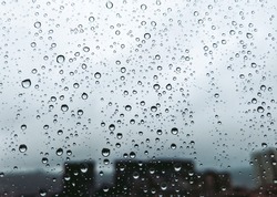 Raindrops on a window with silhouette of buildings in background in a rainy day