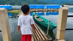 cute asian boy is waiting for the boat on the pier traditional made of bamboo, asia indonesia