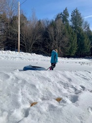 A young girl that is climbing down a mountain while pulling her snow tube behind her. She's dragging the tube with a handle and a thick strap for easy mobility.