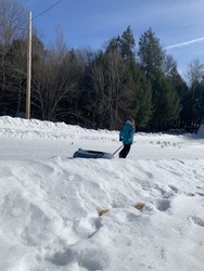 A young girl that is climbing down a mountain while pulling her snow tube behind her. She's dragging the tube with a handle and a thick strap for easy mobility.