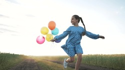 Happy family concept. Child with balloons has fun playing in field in spring. Freedom and childhood dream. Girl run with balloons in sun. Child in wheat field at sunset in summer. Girl playing in park