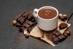 Cup of hot chocolate and pieces of chocolat on dark concrete background