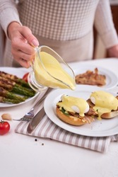 Tasty eggs Benedict - woman pours hollandaise sauce onto poached eggs