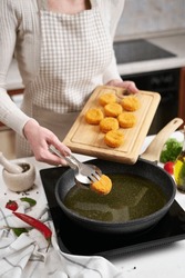 Woman puts cheese balls into frying pan with hot cooking oil