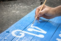 A hand writing signs board with a brush of watercolors on cement floor background. Painting on wooden board in thai language for advertising.