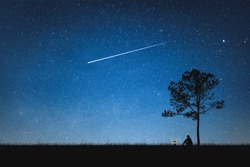 Silhouette of man sitting on mountain and night sky with shooting star. Alone concept.