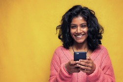 Beautiful Sri Lanka girl makes technology poses with yellow bright background - Young woman uses mobile phone to chatting and messaging