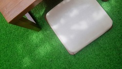 A wooden table and a Japanese seat cushion in a synthetic grass carpet with sunlight rays