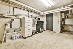 Various storage shelves and cabinet located on shabby floor near pipes and door in cellar