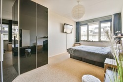 Home interior design of bedroom with bed and wooden wardrobe placed in corner near window in modern apartment