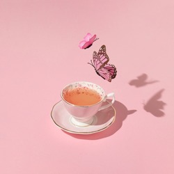 Butterflies flying above vintage cup of tea on pastel pink background. 80s, 90s retro aesthetic romantic spring or summer concept. Minimal fashion love idea.