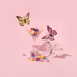 Spring creative layout with colorful butterflies  and martini glasses with dices on pastel pink background. 80s or 90s retro fashion aesthetic  concept. Minimal romantic cocktail idea.