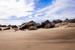 Sandy beach with boulders, large rocks. Blue sky with wispy clouds on a winter's day, Sandy Hook Beach, New Jersey, USA, part of Gateway National Recreation Area, known for hiking, camping, birding.