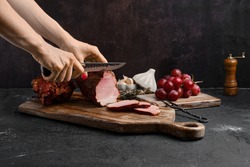 Hands of a woman cut a slice of air dried pork ham on wooden cutting board