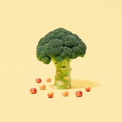 Broccoli tree with fallen apples on pastel yellow background. Healthy food idea. Minimal vegetable and fruit concept.