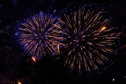Huge fireworks explosions with Violet and golden colors over a party in the park. In front of the black night sky