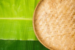 Tampah, winnowing, or nyiru is a tool used for winnowing, namely cleaning rice from husks or other grains of cereal from the skin. banana leaf background. Top view.