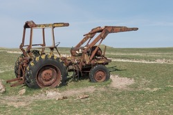 Rusty metal tractor with red and yellow paint peeling off. Abandoned in the middle of the field.
