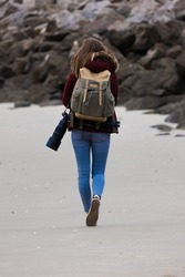 Young attractive female photographer walking on the beach with her camera in winter time