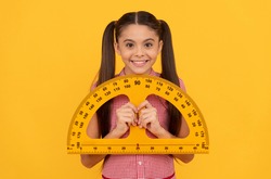 happy teen girl hold school math tool protractor ruler on yellow background, geometry
