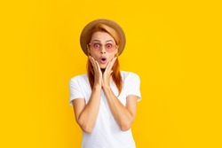 Female model with amazed expression, surprised face. Young redhead woman in straw hat, surprised expression, isolated on yellow background. Summer lifestyle studio portrait.