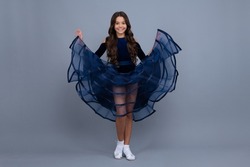 Full length teenager with movement dress. Young teen child with flowing skirt. Teen girl fluttering dress in motion, isolated on gray. Happy girl, positive and smiling emotions.