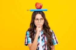 Back to school. Teenager schoolgirl with apple on head, ready to learn. School children on isolated yellow background. Thinking pensive clever teenager girl.