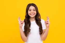 Teenager child holding fingers crossed for good luck. Portrait of cheerful girl prays and hopes dreams come true, crosses fingers for good luck, isolated on yellow studio background.