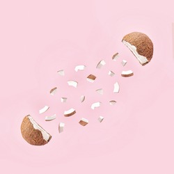 Creative concept of the fresh, organic coconut cut in half with small pieces. Healthy fruit explosion on pastel  pink background.