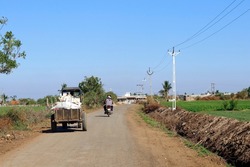 This Photo captured in Indian small village and rural areas in Gujarat India. horizontal road, farm land, small tractor, also motorcyclist and lane of electricity pole beautiful village landscape