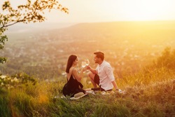 Couple in love on a white plaid take a picnic against the backdrop of a sunset in the mountains. Romantic time. Beautiful couple is enjoying picnic time at sunset.  Copy space.