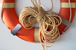 Coiled rope on a boat. Yellow rope and an orange lifebuoy on white wall of a sailboat of marina. Classic yacht or nautical vessel lifeguard resque equipment. 