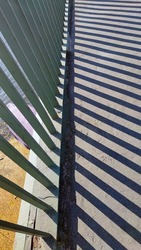 Iron railings of the pedestrian bridge. Autumn sunny day. The bridge has metal railings with parallel vertical balusters. The sun casts a shadow on a gray surface in the form of many lines.