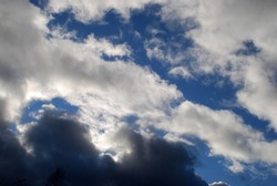 White gray cumulus clouds. Autumn day low fluffy clouds float across the sky. They are snow-white above and dark almost black below due to sunlight and cloud density. Behind them is a blue sky.
