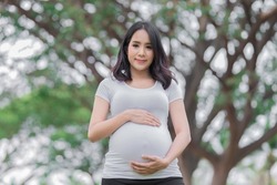 Portrait of asian Beautiful pregnant woman at the park,Thailand people,Happy woman concept,Her use hand touch her belly,Mother day concept