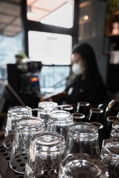 An Array of Clean Glasses in a Coffee Shop with a Female Cashier on the Background
