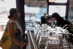 An Array of Clean Glasses in a Coffee Shop with a Cashier Serving a Female Customer on the Background