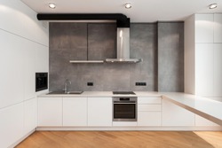 White cupboard with built in household appliance, electric stove, oven, sink on worktop, wooden laminate on floor and extractor hood on grey wall. House with modern interior at contemporary kitchen