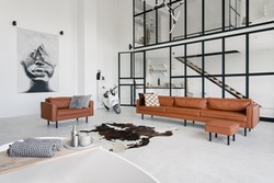 Loft style interior in house with modern living room, bath in bathroom, comfortable couch, pillows on leather armchair, painting on wall and scooter on concrete floor with skin carpet