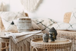 Selective focus at two Buddha statue standing on bamboo coffee table in bright living room interior at bohemian style. Concept mental health and recreation. House with natural materials furniture