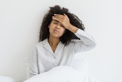 Healthcare concept. Sick afro american woman with closed eyes touch forehead, suffering from headache, sitting on bed in pajamas. Young female feeling unhealthy, strong sudden pain, morning hangover