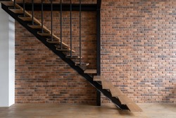 Wooden stairs in modern loft styled room. Modern building with brick wall inside. Modern office for rent. Industrial style room. Multistorey apartment
