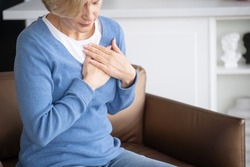 Concept of health problems, cardiovascular and cardiac disease. Cropped view of mature woman feeling heart pain and chest tightness, trying to relieve symptom of arrhythmia
