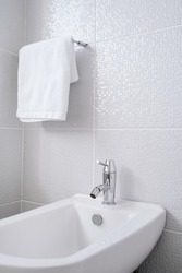 Cropped view of white ceramic bidet and towel in bathroom in Scandinavian style. Personal hygiene. Contemporary washroom interior design. Hotel room facilities