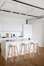 Side view of contemporary kitchen interior design in Nordic style with bar chairs. Spacious and bright apartment. Kitchen appliances and stylish white furniture