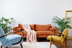 Concept interior design in the style of the 80s. Front view of elegant living room with vintage orange sofa, blue and yellow armchairs. Ergonomic couch in bright apartment with retro interior design